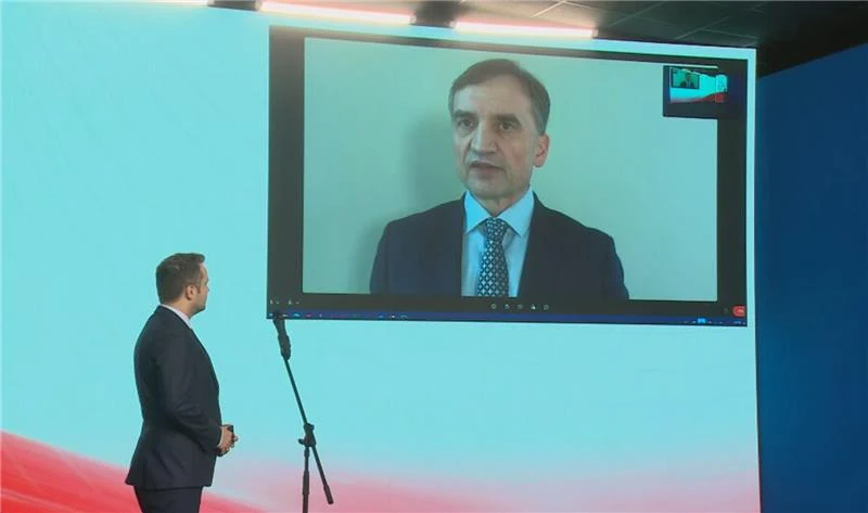 Ziobro stawia warunki rządowi Tuska. Zdalne łączenie z Nowogrodzką Osoba w garniturze widoczna na dużym ekranie podczas wideokonferencji przemawia lub uczestniczy w rozmowie, na pierwszym planie stoi mężczyzna zwrócony w stronę ekranu, w tle profesjonalne studio z mikrofonem.