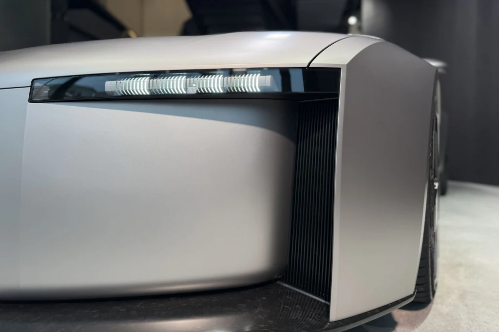 Nowoczesny, matowy samochód o futurystycznej stylistyce z bardzo charakterystycznym prostym i wyrazistym reflektorem LED, zbliżenie na przedni lewy narożnik pojazdu.