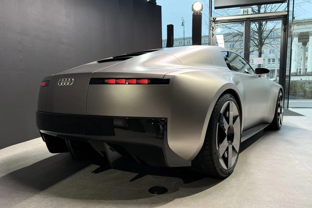 Luksusowy samochód sportowy marki Audi o futurystycznym, aerodynamicznym designie, srebrnym lakierze i charakterystycznych światłach LED, zaparkowany w minimalistycznym, przeszklonym wnętrzu.