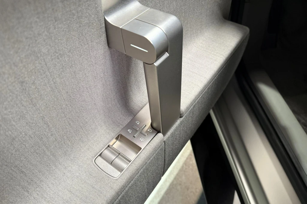Nowoczesny, srebrny uchwyt drzwiowy z przyciskami sterowania w bocznej części drzwi samochodu, otoczony jasnoszarą tapicerką.