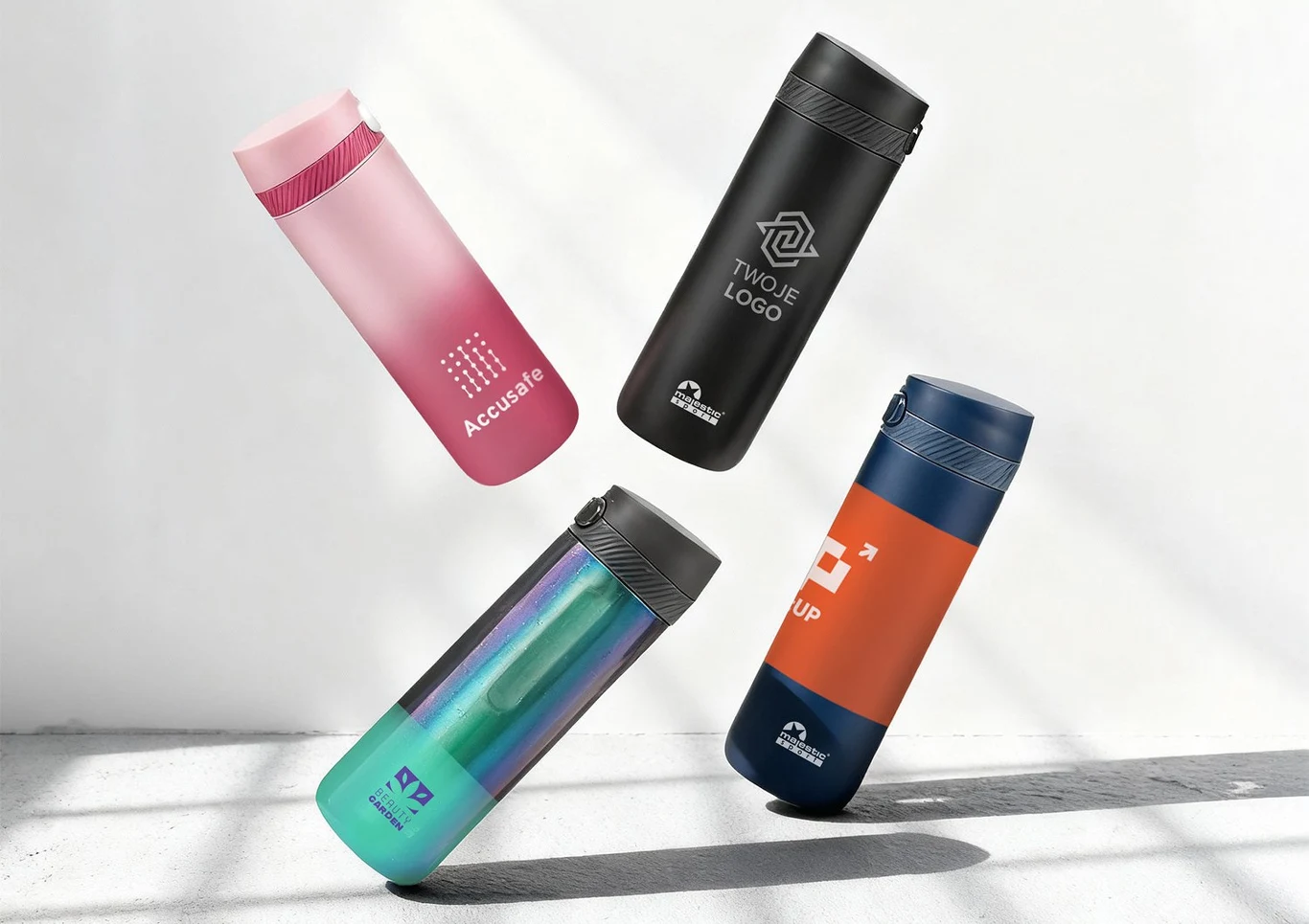 Cztery kolorowe butelki termiczne unoszą się w powietrzu na jasnym tle. Każda z butelek ma inny kolor i nadruk, sugerujące możliwość personalizacji produktu.