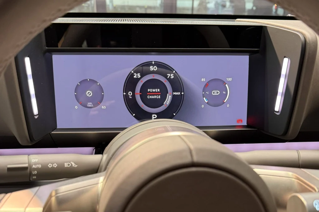 Cyfrowy wyświetlacz zestawu wskaźników samochodowych z centralnym wskaźnikiem mocy i ładowania, po bokach znajdują się zegary informujące o stanie energii i naładowania akumulatora.