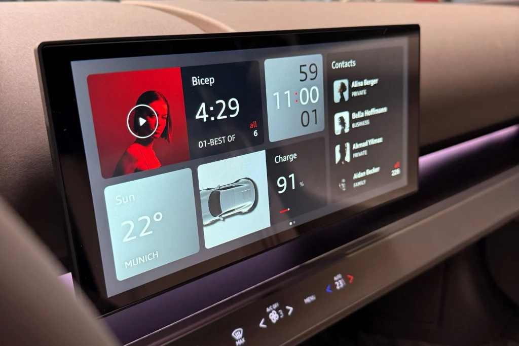 Nowoczesny wyświetlacz samochodowy pokazujący odtwarzacz muzyki, poziom naładowania baterii, godzinę, pogodę w Monachium oraz listę kontaktów.