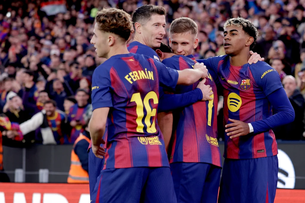 Piłkarze FC Barcelona Czterech piłkarzy FC Barcelony w granatowo-bordowych strojach świętuje zdobycie gola, otoczeni przez rozentuzjazmowanych kibiców na stadionie.