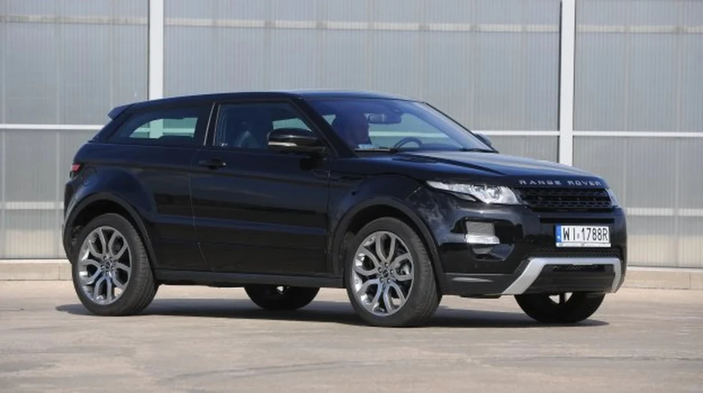 Czarny SUV Range Rover Evoque zaparkowany na tle industrialnego, szklanego budynku. Samochód posiada srebrne felgi, widoczne detale karoserii oraz czytelne tablice rejestracyjne.