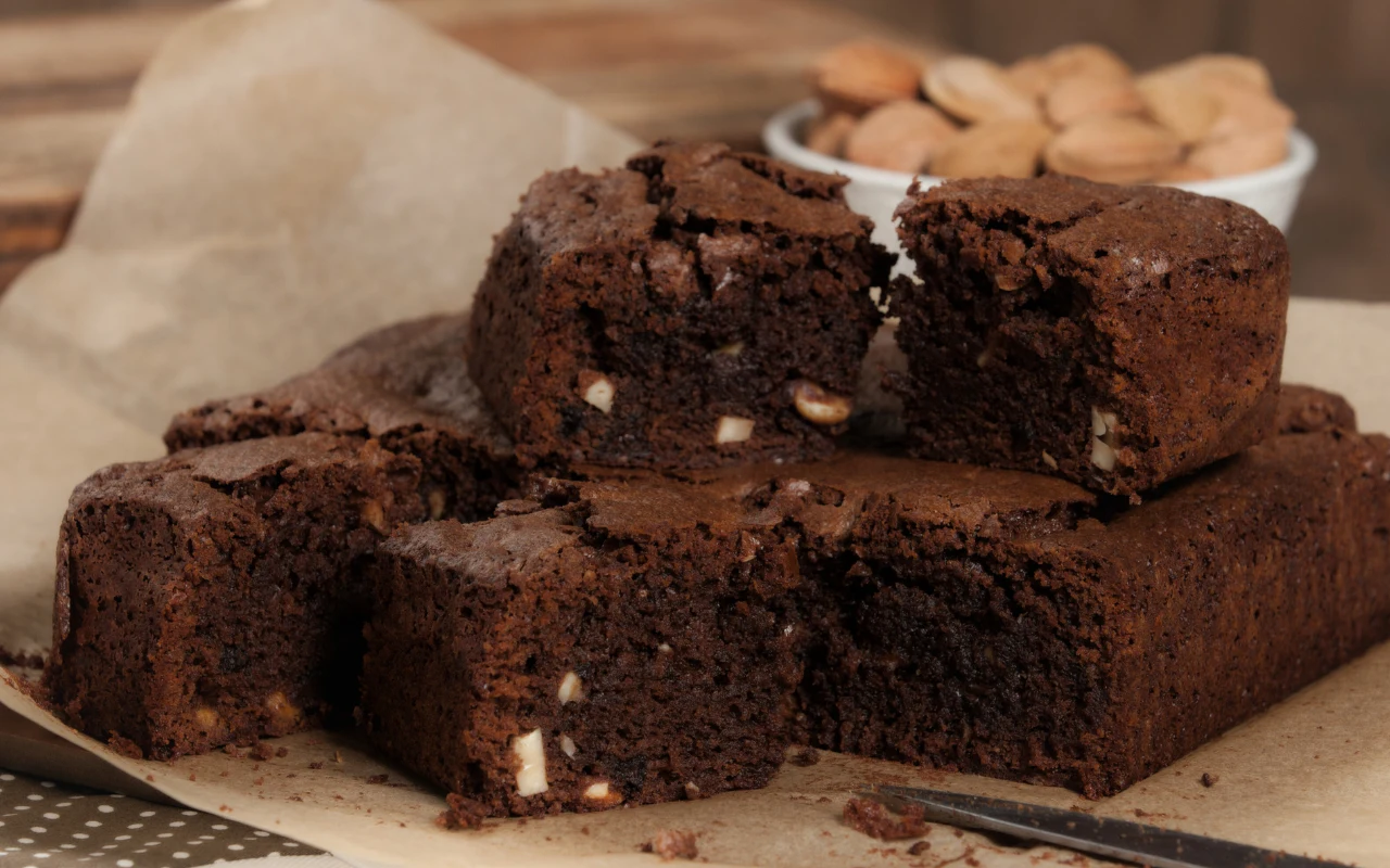 Bolo de mel - świąteczne ciasto z Madery Kawałki wilgotnego ciasta czekoladowego z drobnymi kawałkami orzechów na papierze do pieczenia, w tle miseczka z całymi migdałami.