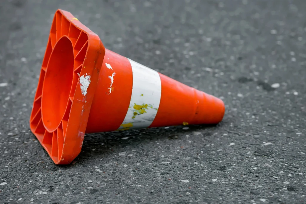 Przewróconego pachołka lepiej nie stawiać. Dlaczego? Leżący na asfalcie pomarańczowy pachołek drogowy z białym paskiem i śladami zużycia.