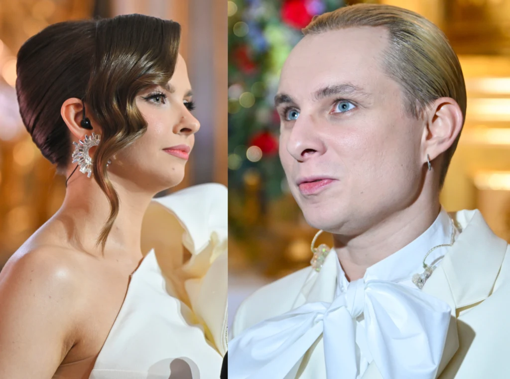 Elegancko ubrana kobieta z ciemnymi włosami upiętymi w gładką fryzurę i dużą ozdobną kolczykiem oraz mężczyzna z jasnymi, zaczesanymi do tyłu włosami w białym stroju z dużą kokardą. Obie osoby znajdują się w jasnym, dekoracyjnym otoczeniu.