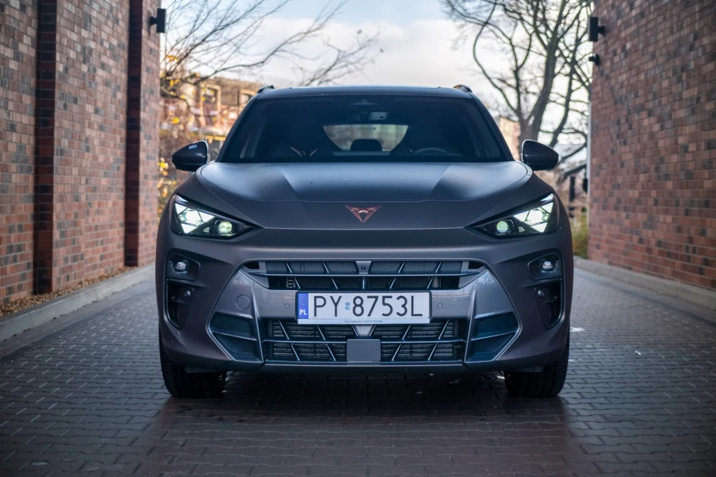 Test CUPRY Terramar 2.0 TSI 4Drive. Klasyczny napęd w nowym SUV-ie Nowoczesny, sportowy samochód marki Cupra w kolorze matowym granatowym zaparkowany przodem między dwoma ceglastymi ścianami, z widoczną tablicą rejestracyjną PY 8753L oraz włączonymi światłami do jazdy dziennej.