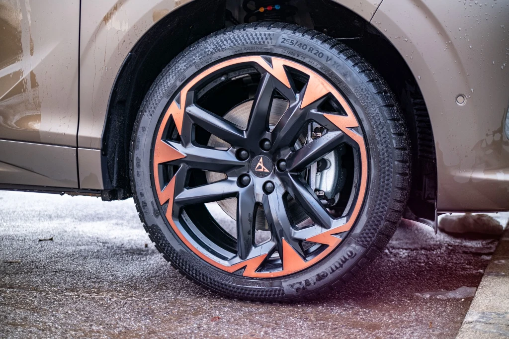 20-calow obręcze wymagają dopłaty 6,3 tys. zł. Zimowe Continentale trzymają się asfaltu jak przyklejone Duże czarne felgi aluminiowe z pomarańczowymi akcentami na oponie niskoprofilowej zamontowanej w samochodzie w kolorze beżowym, widoczne detale bieżnika i fragment nadkola na tle mokrego asfaltu.
