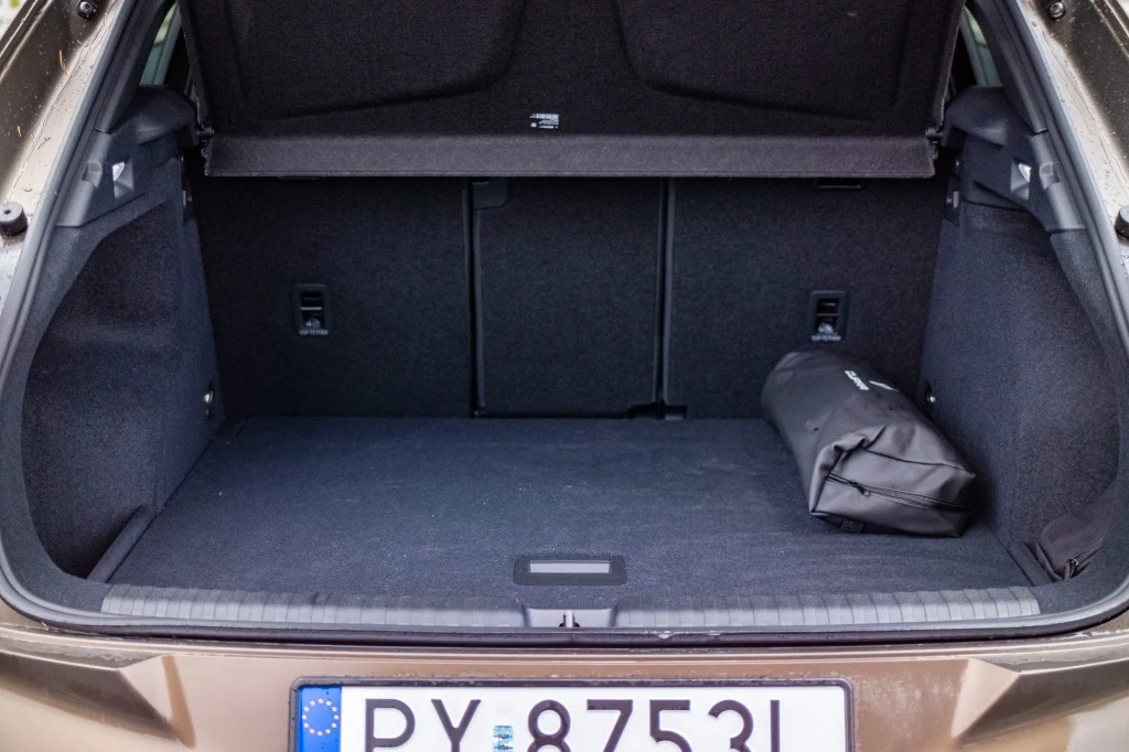 Bagażnik ma standardowo 540 l pojemności. Przesuwając kanapę można dołożyć jeszcze 90 l. Otwarty bagażnik samochodu z czarną tapicerką, częściowo widoczną tablicą rejestracyjną oraz zapakowaną torbą lub zestawem naprawczym umieszczonym z prawej strony.