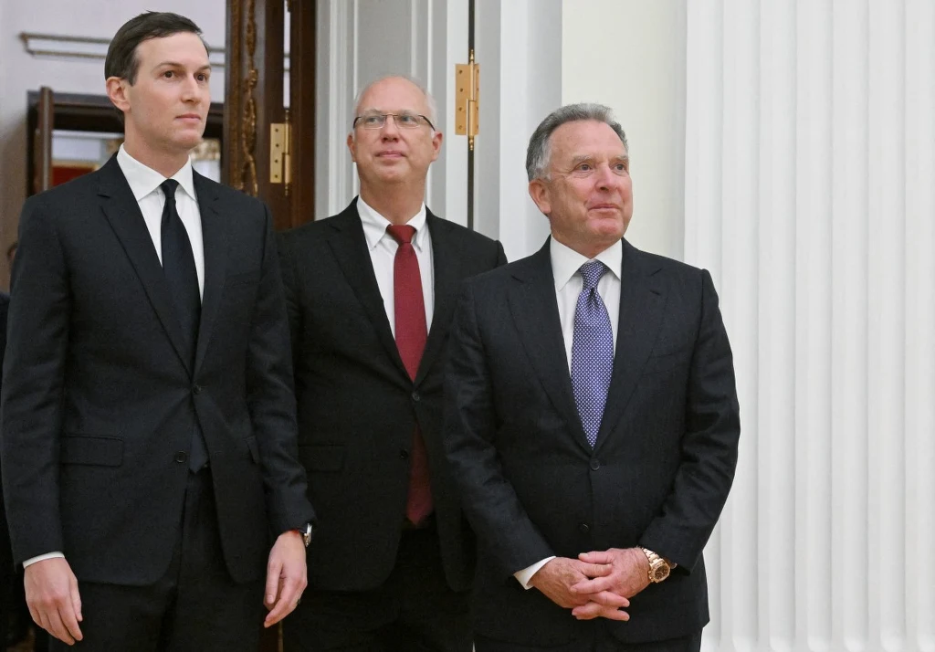 Jared Kushner (L) i Steve Witkoff (P) w towarzystwie doradcy Władimira Putina Kiryła Dmitriewa (Ś) Trzech mężczyzn ubranych w garnitury stoi w oficjalnym wnętrzu, dwaj mają krawaty, a jeden z nich nosi okulary. W tle widać fragment drzwi oraz białą kolumnę.