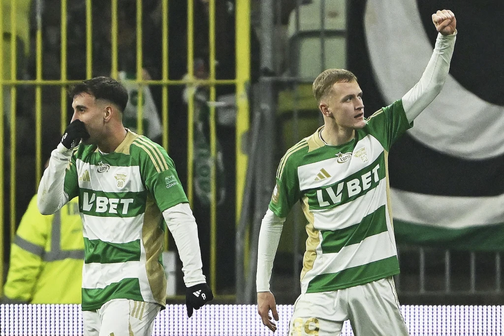 Snajperski wieczór na Polsat Plus Arena Gdańsk rozpoczął Tomasz Bobczek (na zdj. z prawej) Dwóch piłkarzy w zielono-białych strojach drużyny Lechii Gdańsk świętuje sukces na boisku sportowym, jeden z nich unosi zaciśniętą pięść w górę, w tle widoczny fragment trybun i kibice.