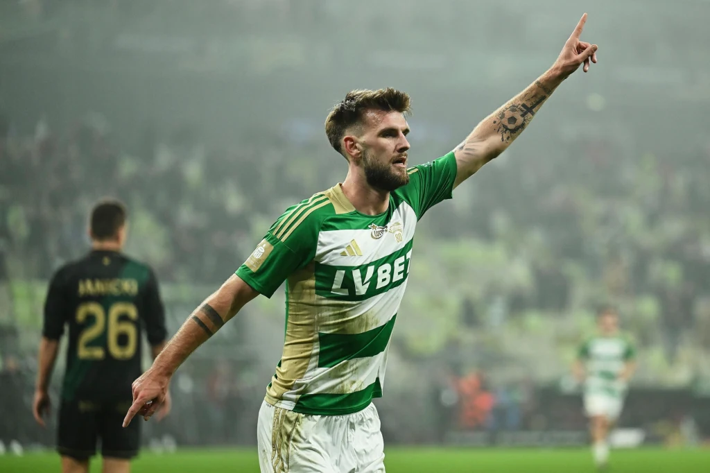 Kacper Sezonienko dwukrotnie kierował piłkę do siatki w doliczonym czasie gry Piłkarz w zielono-białej koszulce z uniesioną ręką świętuje zdobycie bramki na stadionie, w tle rozmyci zawodnicy i kibice.