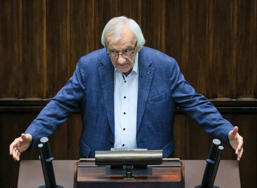 Ryszard Terlecki przeprosił w Sejmie Sławomira Nitrasa Mężczyzna w siwych włosach, ubrany w niebieską marynarkę i jasną koszulę, stoi za mównicą w przestrzeni przypominającej salę obrad parlamentu, z rozłożonymi rękami, patrząc w dół.