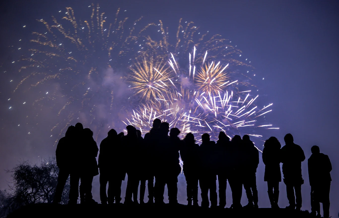 Polacy chętnie wyjeżdżają na Sylwestra Sylwetki grupy ludzi stojących na wzniesieniu, obserwujących nocny pokaz fajerwerków na tle rozświetlonego nieba.