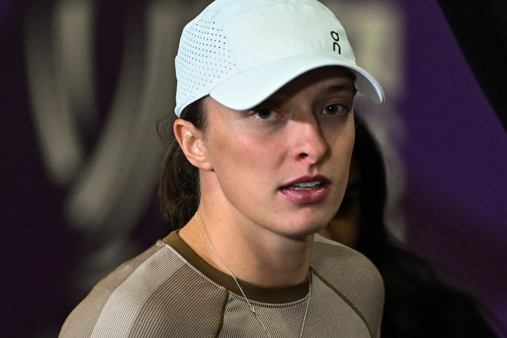 Iga Świątek ponownie rozpocznie sezon od United Cup Młoda kobieta w jasnej czapce z daszkiem i sportowej bluzie, spogląda przed siebie na tle rozmytego, ciemnego tła.