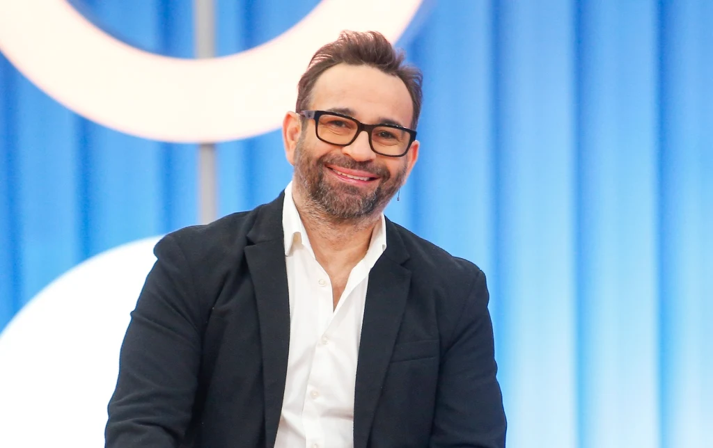 Stylista fryzur Maciej Maniewski w białej koszuli i czarnej marynarce, uśmiechnięty