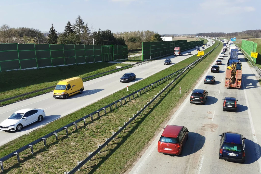 W Hiszpanii 85 proc. kierowców jeździ po drogach samotnie. Władze chcą z tym walczyć Samochody poruszające się dwupasmową autostradą w obu kierunkach, jedna jezdnia jest zatłoczona, druga niemal pusta. Po bokach drogi ustawione są zielone ekrany dźwiękochłonne, a w tle widoczne są drzewa i niebo.