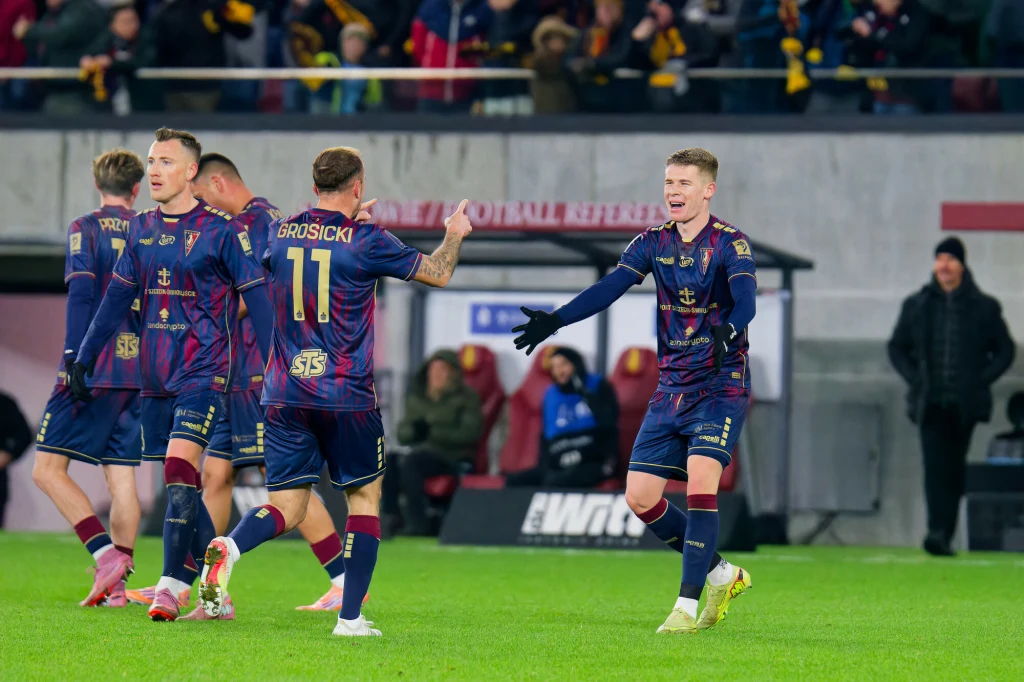 Pogoń Szczecin - Radomiak Radom Zawodnicy drużyny piłkarskiej w granatowo-bordowych strojach cieszą się ze zdobytego gola na boisku, niektórzy przybijają sobie piątki, w tle widoczna jest publiczność oraz stadion.