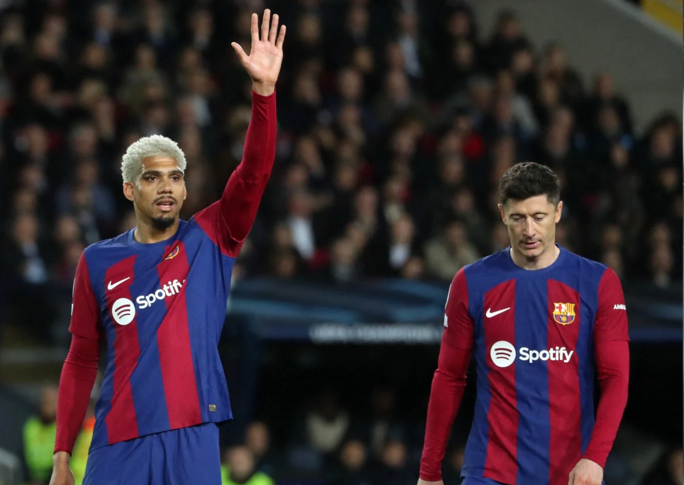 Ronald Araujo i Robert Lewandowski Dwóch piłkarzy FC Barcelony w granatowo-bordowych strojach z logotypem Spotify, jeden z nich z uniesioną ręką, na tle trybun wypełnionych kibicami.