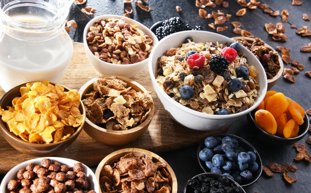 Najbardziej zanieczyszczone są płatki śniadaniowe - wynika z najnowszych testów Różne rodzaje płatków śniadaniowych i musli ułożone w miseczkach, wśród których znajduje się mleko i świeże owoce jak borówki, maliny, jeżyny oraz suszone morele. Całość tworzy apetyczną i kolorową kompozycję śniadaniową.