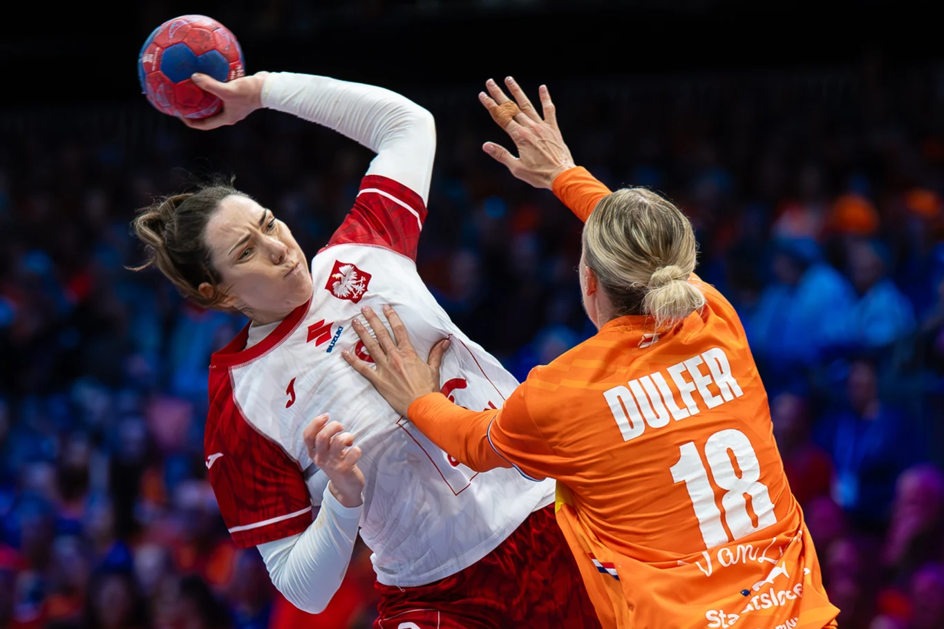 Monika Kobylińska i Kelly Dulfer. 10 lat temu grały o finał mistrzostw świata, dziś rywalizowały o ćwierćfinał Zawodniczka w białoczerwonym stroju drużyny Polski wykonuje rzut podczas meczu piłki ręcznej, blokowana przez rywalkę w pomarańczowym stroju z napisem Dulfer i numerem 18. Tło wypełniają rozmazani kibice.