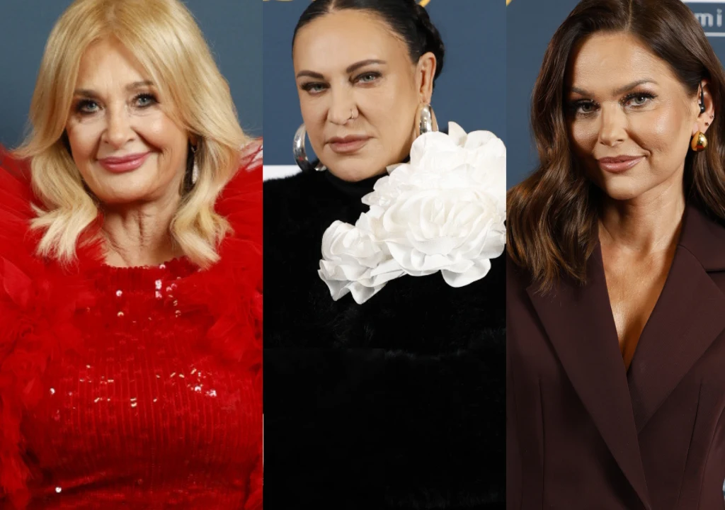 Trzy kobiety ustawione obok siebie, ubrane w eleganckie stroje wieczorowe, każda patrzy prosto w obiektyw. Blondynka w czerwonej sukni z piórami, kobieta w czerni z ozdobą w postaci białego kwiatu oraz brunetka w garniturze w kolorze bordo.