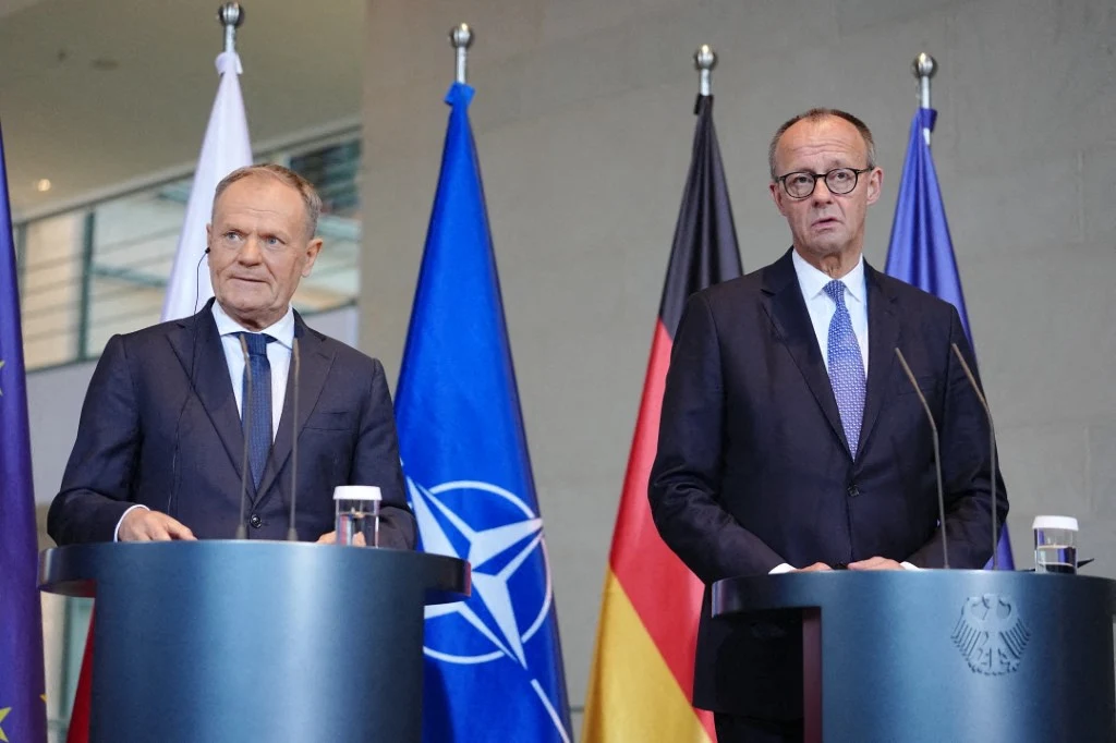 Dwóch mężczyzn w garniturach stoi przy pulpitach na tle flag Polski, NATO i Niemiec, prowadząc wspólną konferencję prasową.