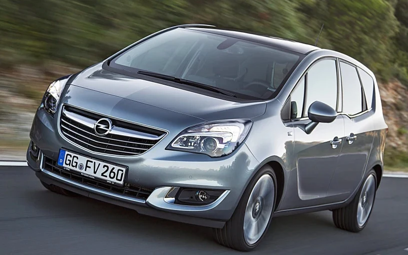 Wśród piętnastu najlepszych ośmio- i dziewięcioletnich samochodów według TÜV znalazło się miejsce dla Opla Merivy z końcowej fazy produkcji Srebrny Opel Meriva II w ruchu na asfaltowej drodze, widoczne reflektory, znak firmowy na masce oraz niemiecka tablica rejestracyjna, tło rozmyte z powodu jazdy.