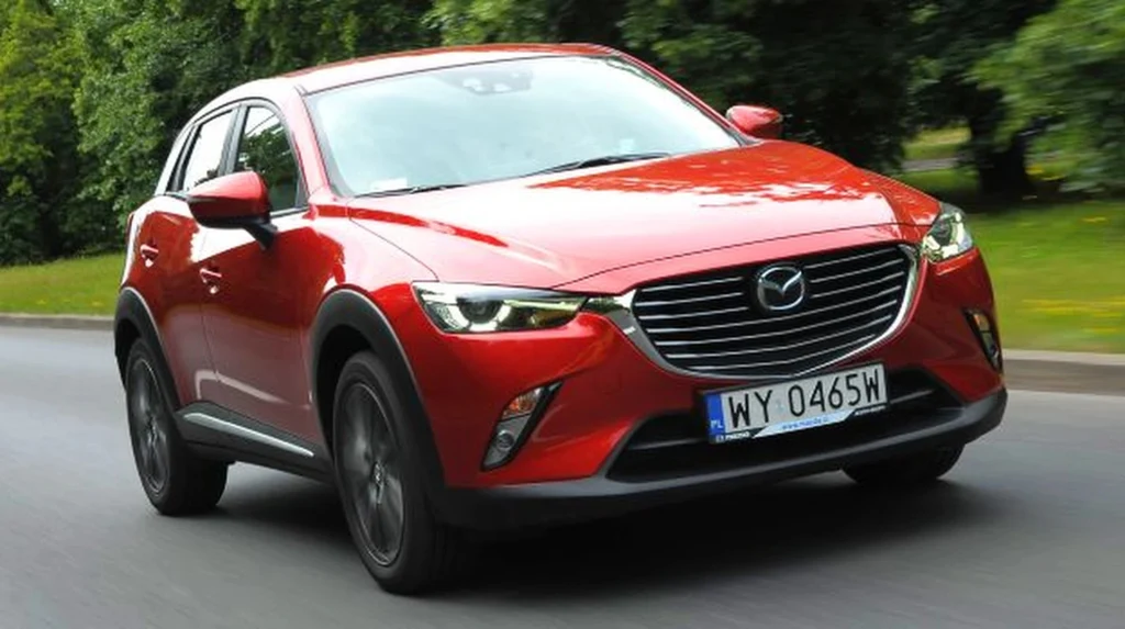W przypadku Mazdy CX-3 warto zwrócić uwagę na tarcze hamulcowe Czerwony samochód Mazda CX-3 z polską tablicą rejestracyjną na jezdni, otoczony zielenią drzew w tle.