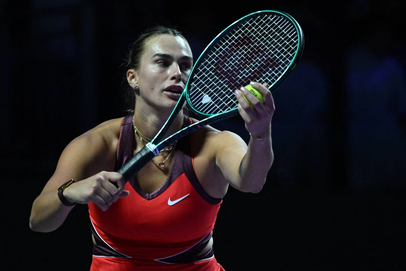 Aryna Sabalenka Tenisistka w dynamicznej pozie podczas serwisu, ubrana w czerwony strój sportowy, skupiona na precyzyjnym uderzeniu rakietą tenisową, światło podkreśla sportową atmosferę kortu.