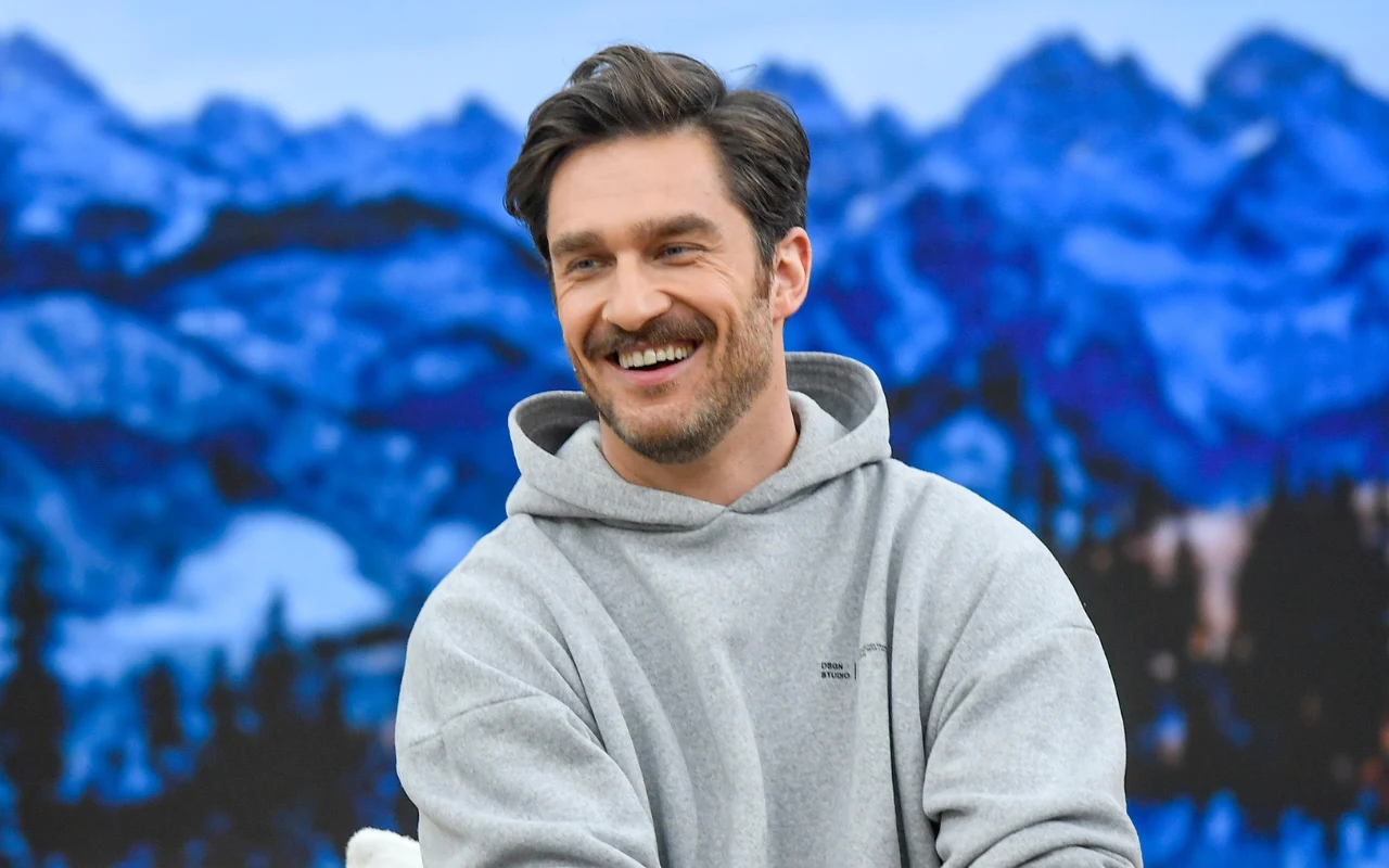 Uśmiechnięty mężczyzna z zarostem w szarej bluzie z kapturem