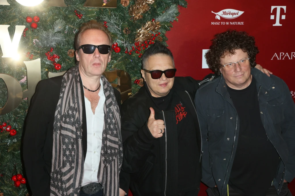 W składzie T.Love nie ma już Jana Benedka (z lewej) i Sidneya Polaka (z prawej). W środku lider i wokalista - Muniek Staszczyk Trzech mężczyzn pozuje razem na tle świątecznej dekoracji z zielonych gałęzi i czerwonych ozdób. Wszyscy mają na sobie ciemne ubrania i okulary przeciwsłoneczne, jeden z nich pokazuje gest kciuka w górę.