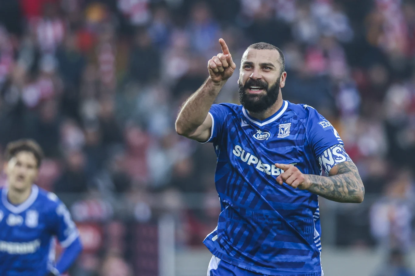 Mistrzowie Polski objęli prowadzenie po bramce Mikaela Ishaka z rzutu karnego Piłkarz w niebieskim stroju drużyny Lech Poznań z wyciągniętym ku górze palcem, wyraża radość po zdobyciu bramki podczas meczu piłkarskiego; w tle rozmyci zawodnicy i fragment trybun.