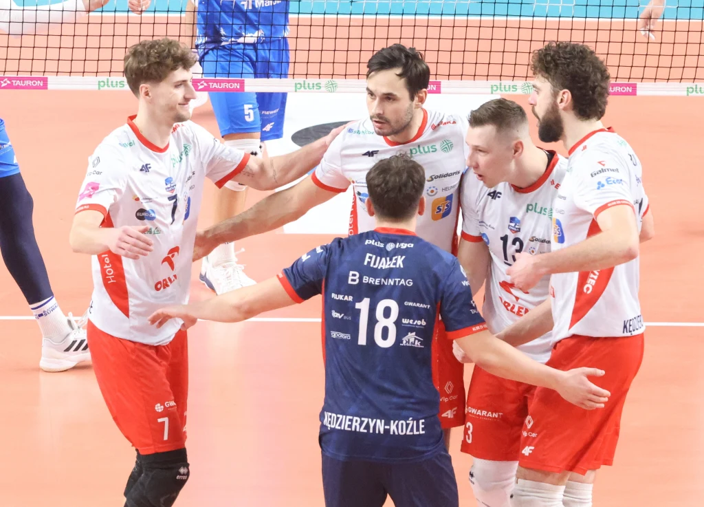 Siatkarze ZAKS-y Kędzierzyn-Koźle Grupa siatkarzy ubranych w stroje sportowe drużyny ZAKSA Kędzierzyn-Koźle celebruje zdobycie punktu na boisku siatkarskim, widoczne emocje oraz współpraca pomiędzy zawodnikami.
