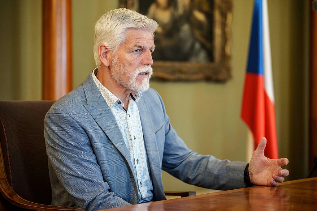 Prezydent Czech Petr Pavel: Nie powinniśmy w żaden sposób osłabiać siły NATO Siwowłosy mężczyzna z brodą ubrany w jasnoszary garnitur siedzi przy drewnianym stole i gestykuluje dłońmi, w tle widoczna czeska flaga oraz obraz w złotej ramie.