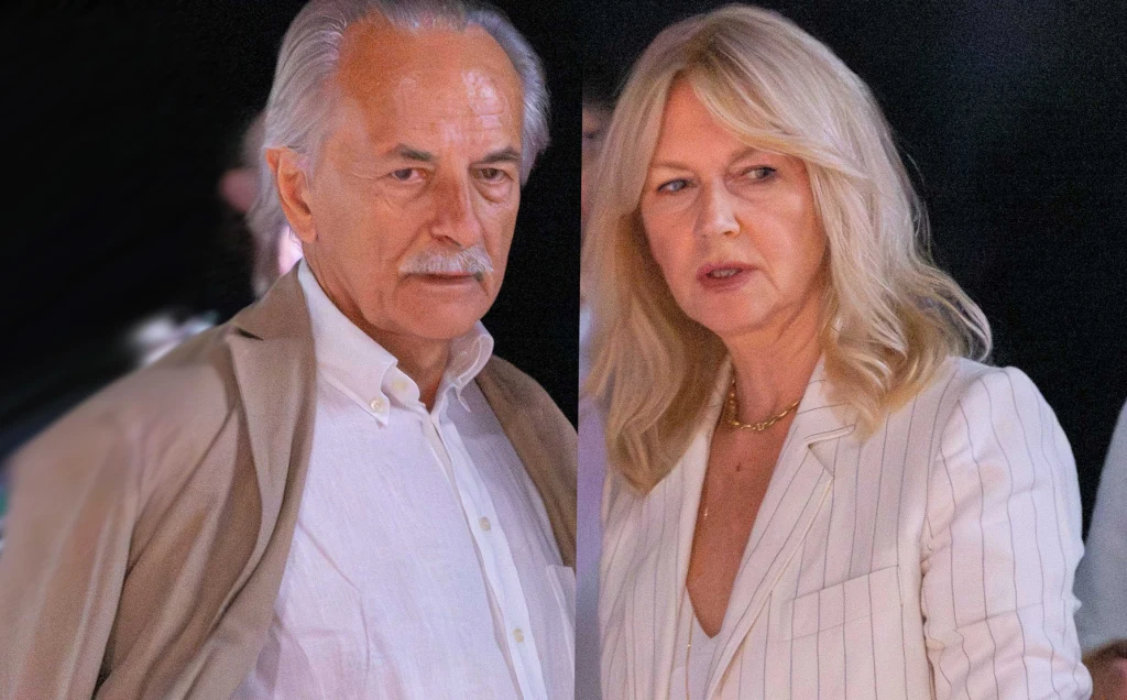 Adam Torbicki i Grażyna Torbicka Starszy mężczyzna o siwych włosach i wąsach w beżowej marynarce oraz kobieta o blond włosach ubrana w jasny garnitur stoją obok siebie, patrząc w kierunku aparatu, tło jest ciemne i rozmyte.