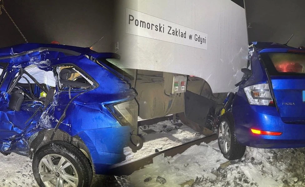 Zderzenie niebieskiego samochodu osobowego z dużym pojazdem lub infrastrukturą, auto zostało poważnie zniszczone, wokół widoczny śnieg i elementy infrastruktury miejskiej. Na ścianie budynku widoczny napis Pomorski Zakład w Gdyni.