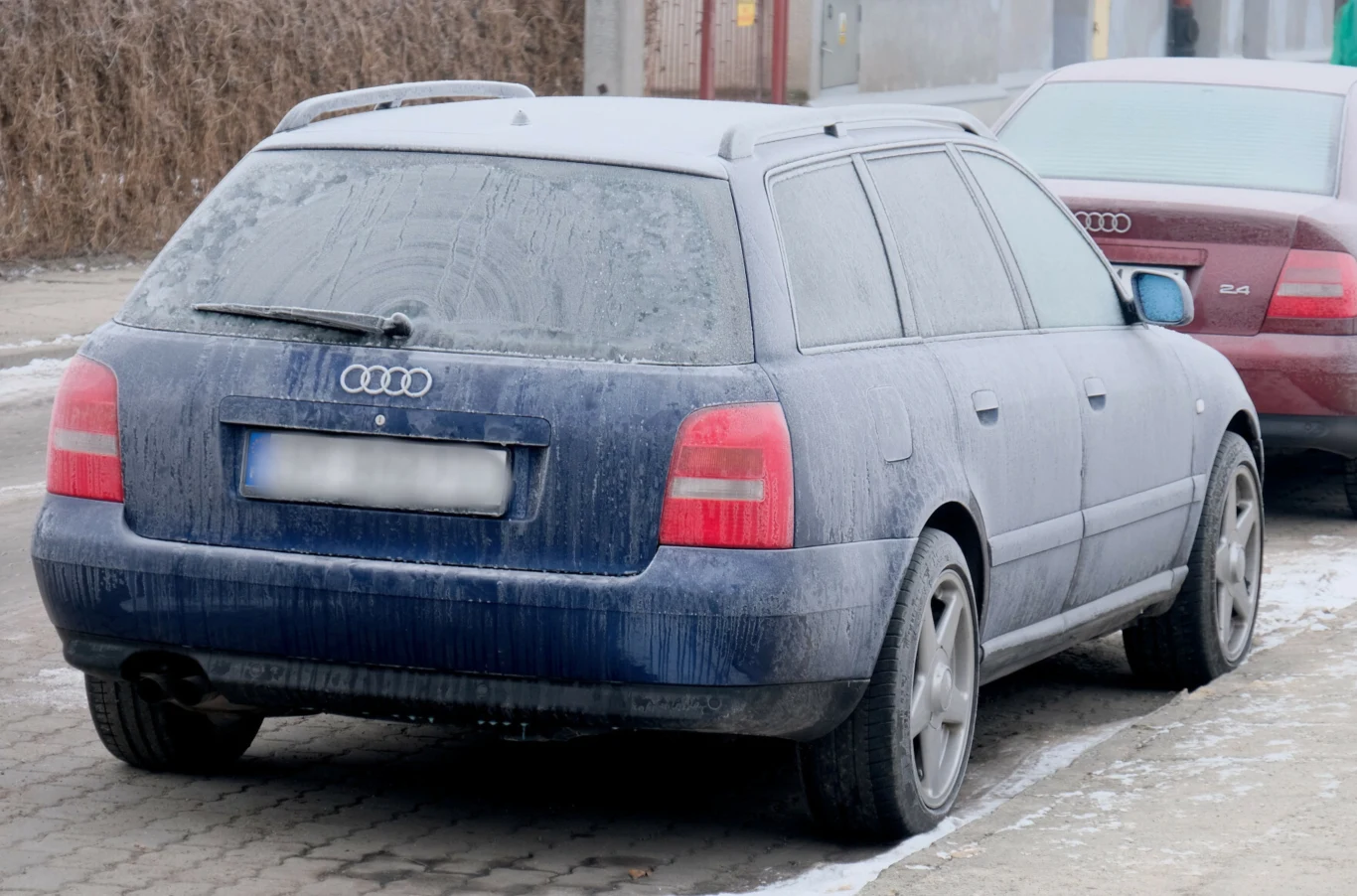 Nadciąga antycyklon Gerd. Temperatura spadnie do nawet -15 st. C. Niebieski samochód marki Audi pokryty warstwą lodu i szronu stoi zaparkowany na ulicy, obok innego auta. Widoczne są zamarznięte szyby i tylna tablica rejestracyjna częściowo zamazana przez szron.