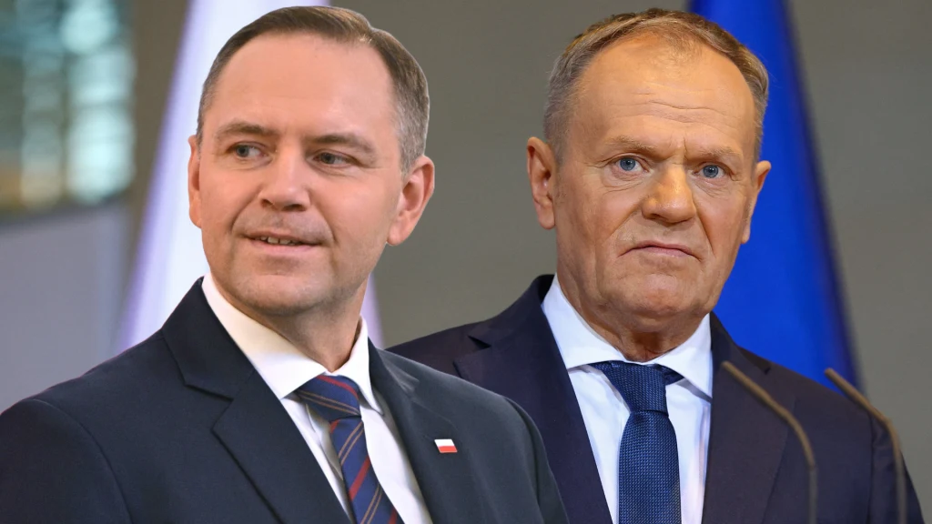 Dwóch mężczyzn w garniturach, jeden uśmiechnięty z widoczną flagą Polski na klapie marynarki, drugi o poważnym wyrazie twarzy na tle błękitnej flagi.