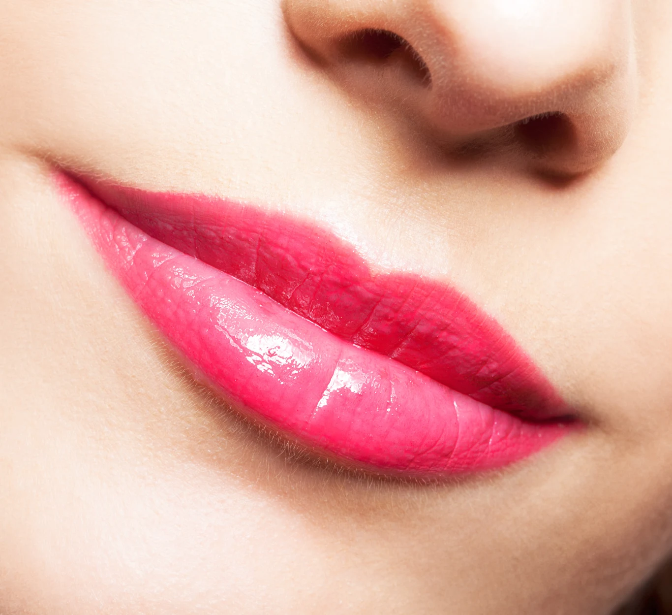 Zbliżenie kobiecych ust z intensywnie różową, błyszczącą pomadką, widoczna gładka skóra i fragment nosa.
