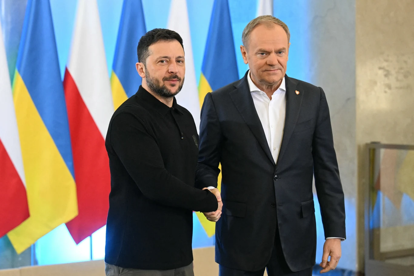 Polska da gwarancje na 10,3 mld euro pod pożyczkę dla Ukrainy w zamrożonych rosyjskich aktywów, jeśli zostanie osiągnięte porozumienie w tej sprawie Dwóch mężczyzn w formalnym stroju ściska sobie dłonie na tle flag Ukrainy i Polski, co sugeruje oficjalne spotkanie polityczne.