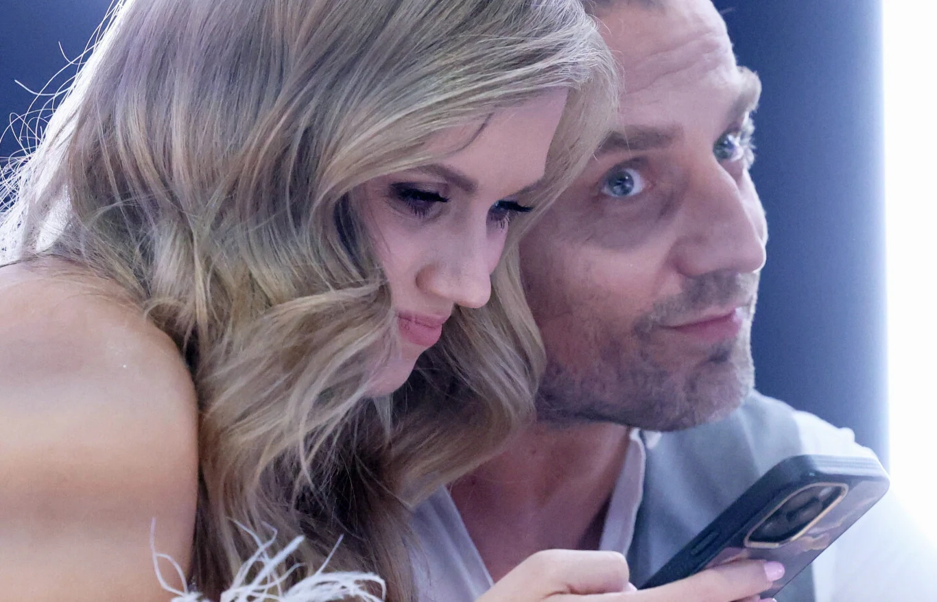 Agnieszka Kaczorowska i Marcin Rogacewicz Dwie osoby siedzą blisko siebie, kobieta trzyma telefon i skupia wzrok na ekranie, a mężczyzna patrzy w bok z lekkim uśmiechem.