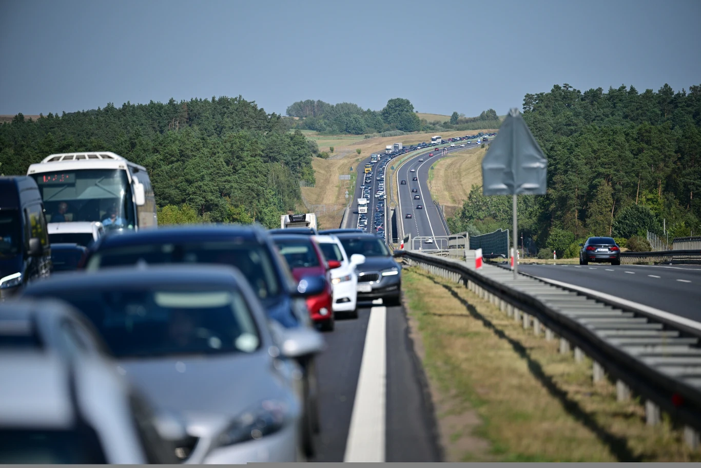 Według Reutersa, 16 grudnia UE ma ogłosić propozycje, które odsuną w czasie zakaz silników spalinowych po 2035 roku Długi korek na autostradzie otoczony zielenią, sznur samochodów stojących w obu kierunkach na dwupasmowej drodze, w oddali widoczny pagórkowaty krajobraz.