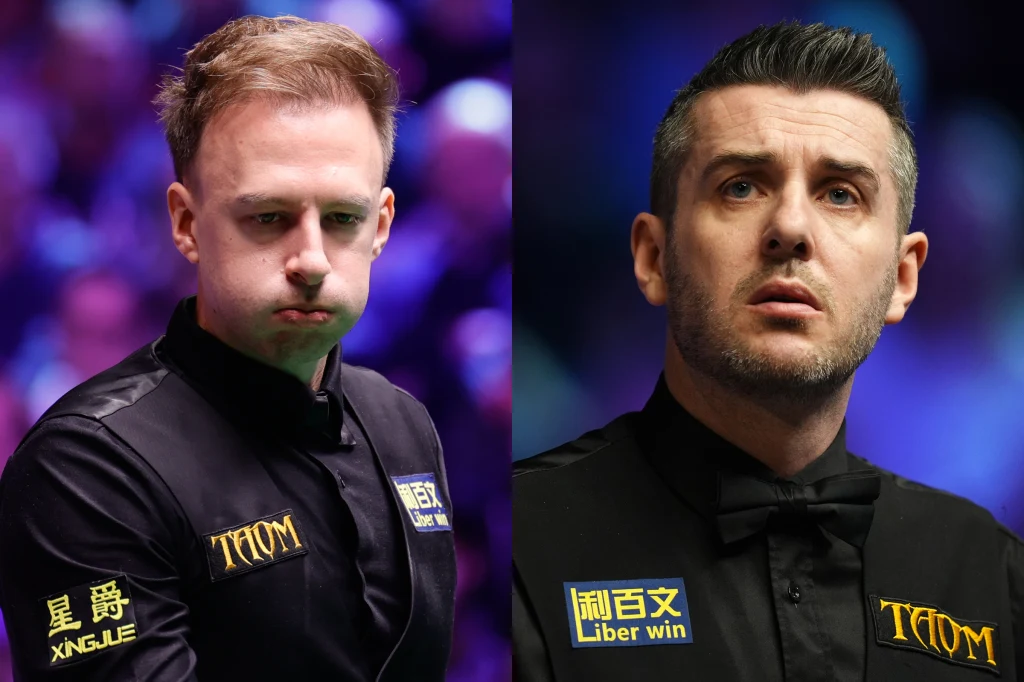 Judd Trump (z lewej) i Mark Selby Dwóch mężczyzn ubranych w eleganckie, czarne kamizelki z naszywkami sponsorów na turnieju snookera, jeden z nich z nadętą miną, drugi skupiony, rozmyte kolorowe tło podkreślające atmosferę sportowego wydarzenia.