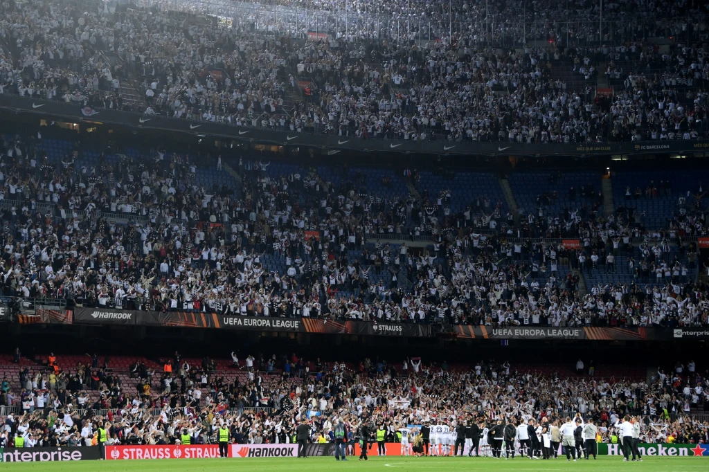 Kibice Eintrachtu Frankfurt na Camp Nou (14.04.2022) Ogromna liczba kibiców w białych koszulkach zajmuje trybuny stadionu podczas meczu piłki nożnej UEFA Europa League, na murawie widoczna jest grupa osób, prawdopodobnie piłkarzy i sztabu szkoleniowego, wokół banery sponsorów i charakterystyczna architek...