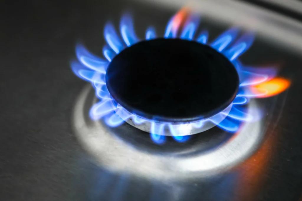 Gaz systematycznie tanieje na światowych rynkach. Czy w przyszłym roku gospodarstwa domowe zapłacą niższe rachunki? Zdj. ilustracyjne Palnik gazowy emitujący niebieski płomień na tle metalowej powierzchni kuchenki.