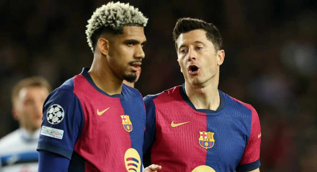 Ronald Araujo i Robert Lewandowski. Czy zagrają jeszcze kiedyś w jednej drużynie? Dwóch piłkarzy FC Barcelony w granatowo-bordowych koszulkach rozmawia ze sobą podczas meczu, widoczne są wyraźnie loga klubu oraz Liga Mistrzów.