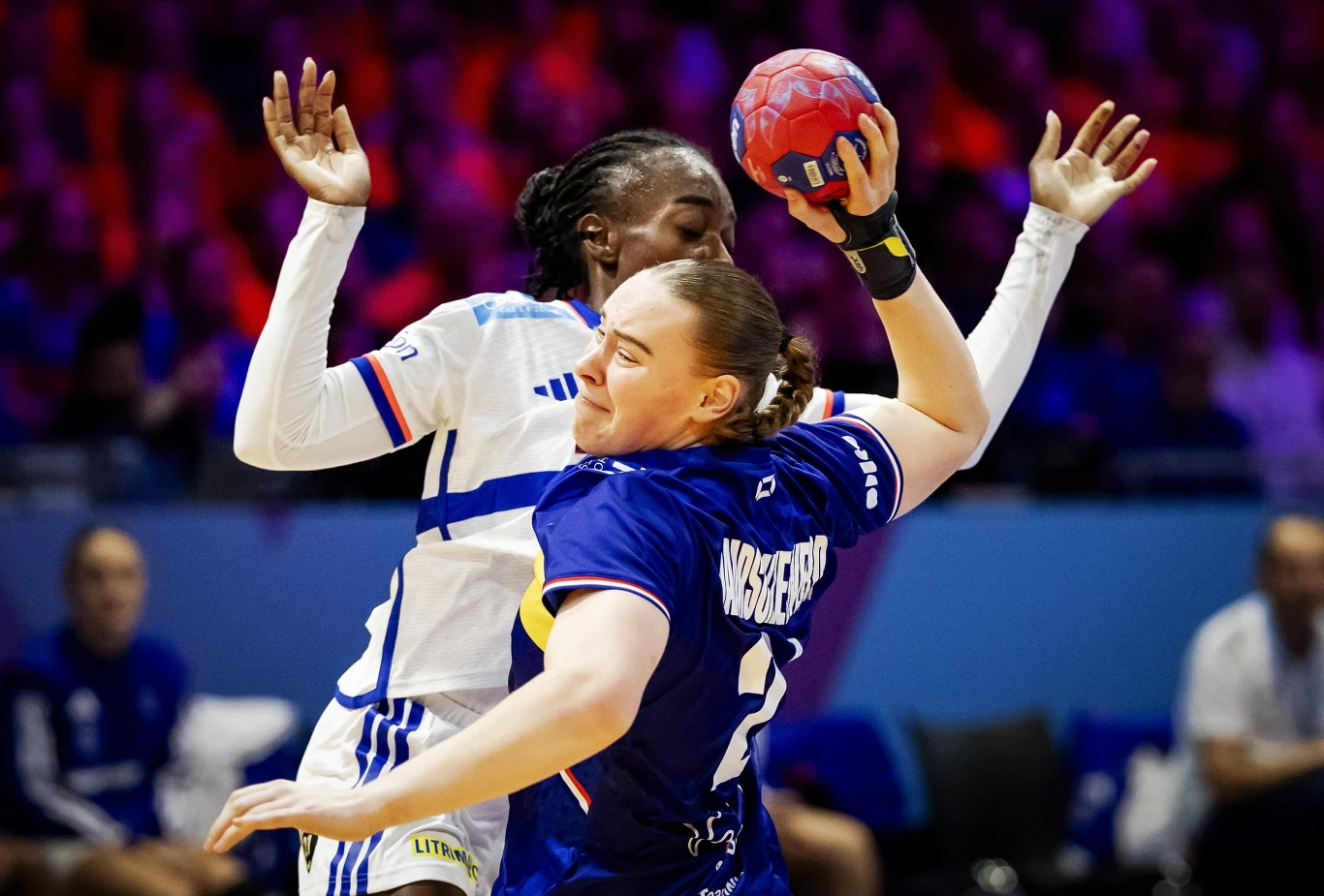 Rzuca Romee Maarschalkerweerd, broni Onacia Ondono. Pasjonujący mecz Danii z Francją Dwie zawodniczki w trakcie dynamicznej akcji podczas meczu piłki ręcznej, jedna z nich trzyma piłkę i próbuje przedostać się obok rywalki, intensywna rywalizacja sportowa, w tle rozmyte postacie widzów i trenerów.